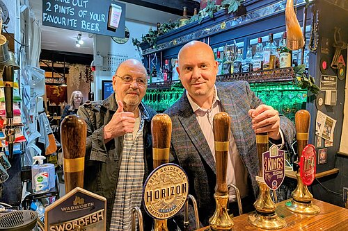 Cameron stands behind a bar pouring a pint